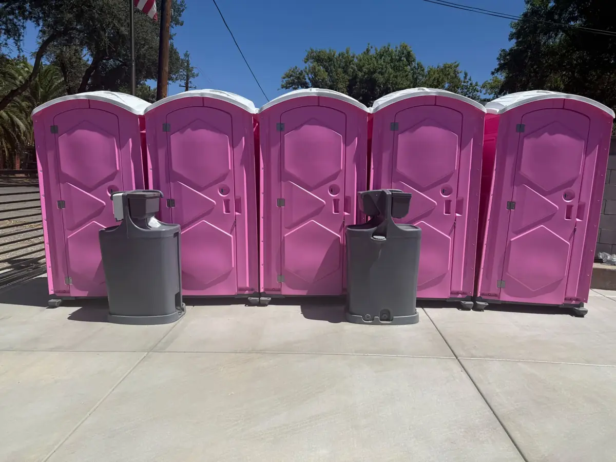Row of pink porta potties with two grey hand-wash stations in front