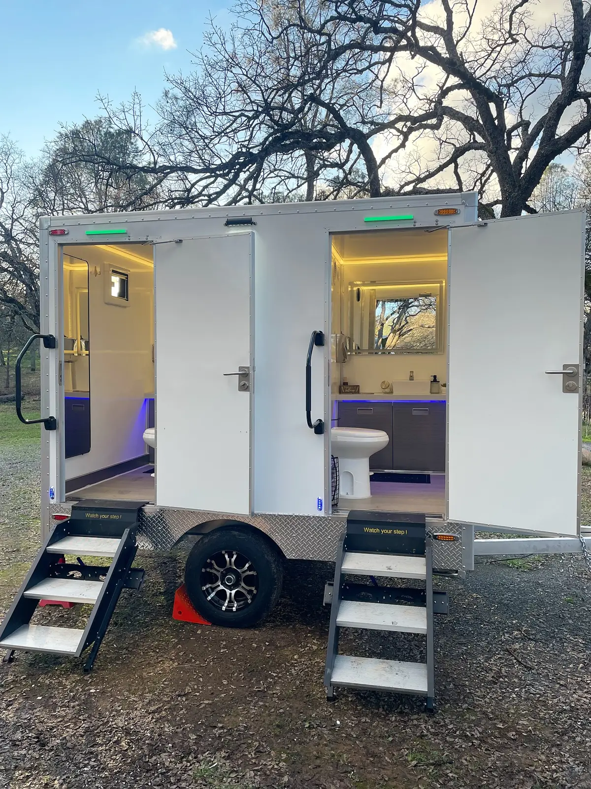 Two-stall restroom trailer with both doors open and lit vanities inside