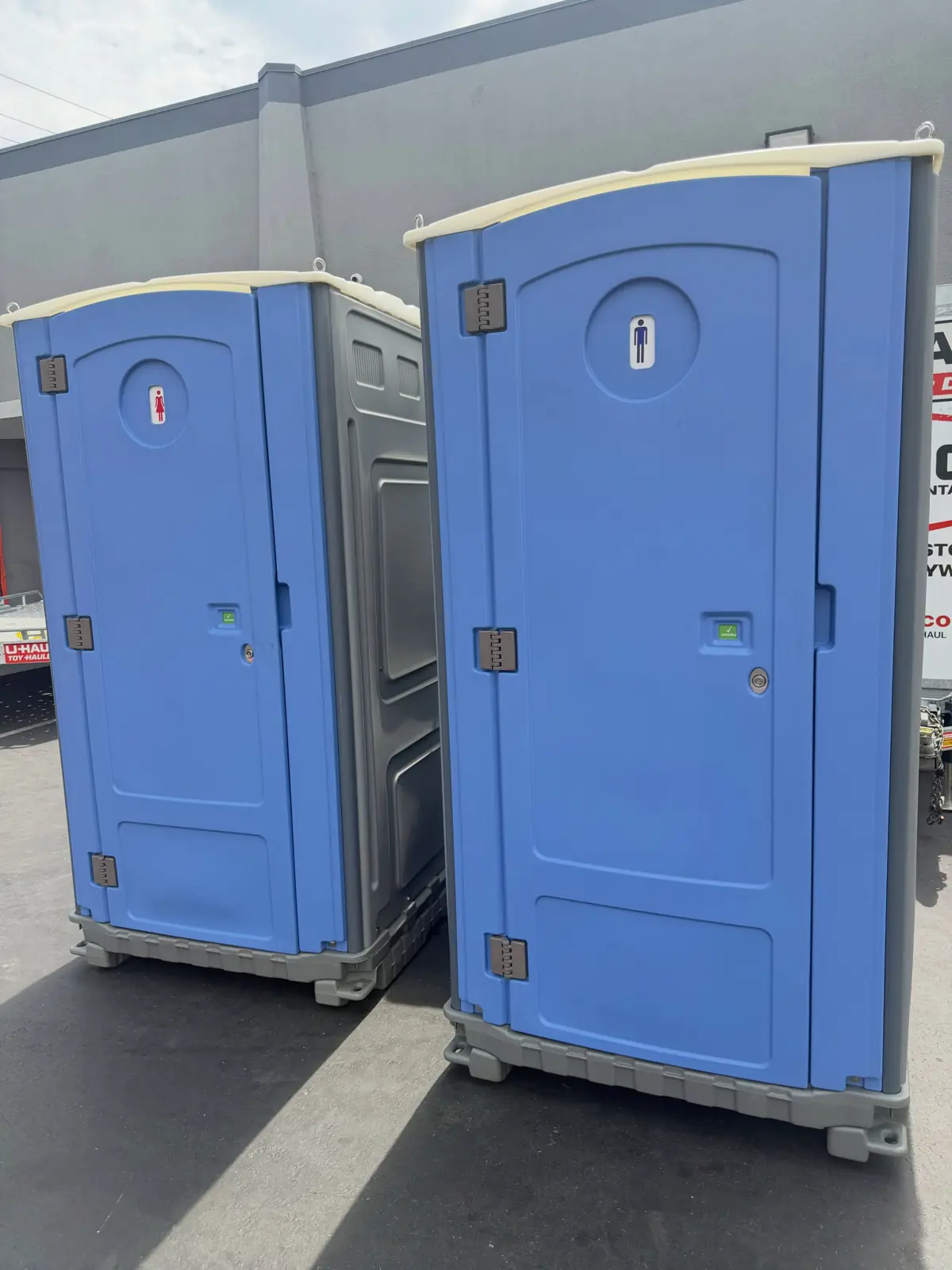 Two blue standard porta potties side by side on a paved lot
